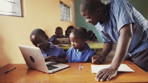4k of teacher instructing African school students / pupils to use laptop computer in classroom.