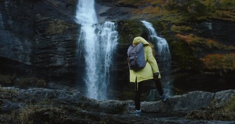 CINEMAGRAPH - SEAMLESS LOOP. Caucasian female hiker in yellow raincoat enjoys the view of a beautiful waterfall in French Alps วิดีโอสต็อก
