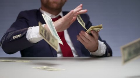 Wealthy businessman throwing bills out of a bundle money on table. Rish man holding in hands bundle dollars and spending large sums money