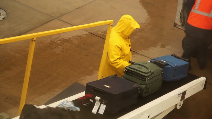 Baggage handlers load luggage onto an airplane in the rain.