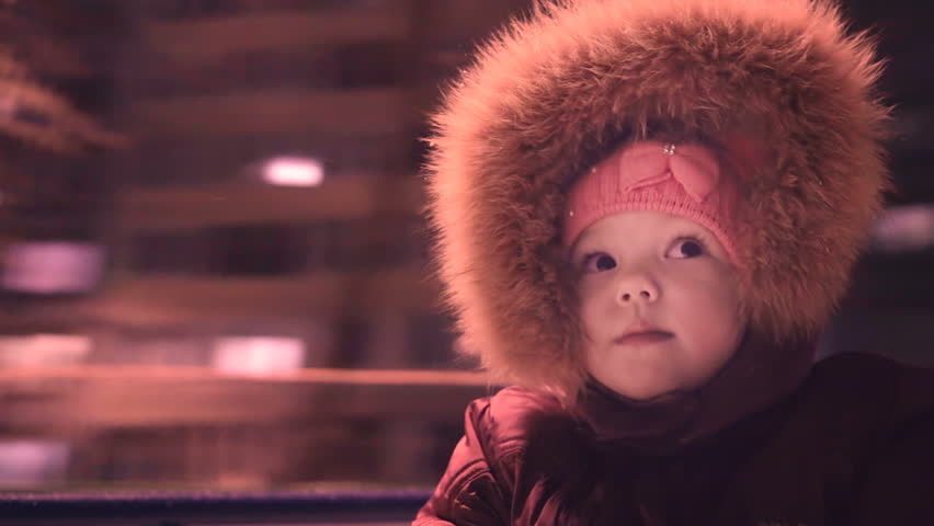A sweet girl is spinning on the carousel. Nearby is Mom and Dad.