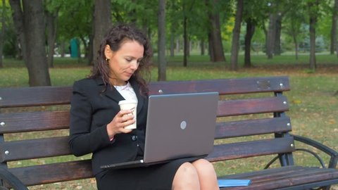 Girl with laptop drinking coffee in the park.