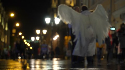 Man in costume love Angel Cupid on night city streets and lovers couples. Concept Christmas, New year, Valentine's day, carnival. Angel holds bow and lit Sparkler and makes selfie with couples in love