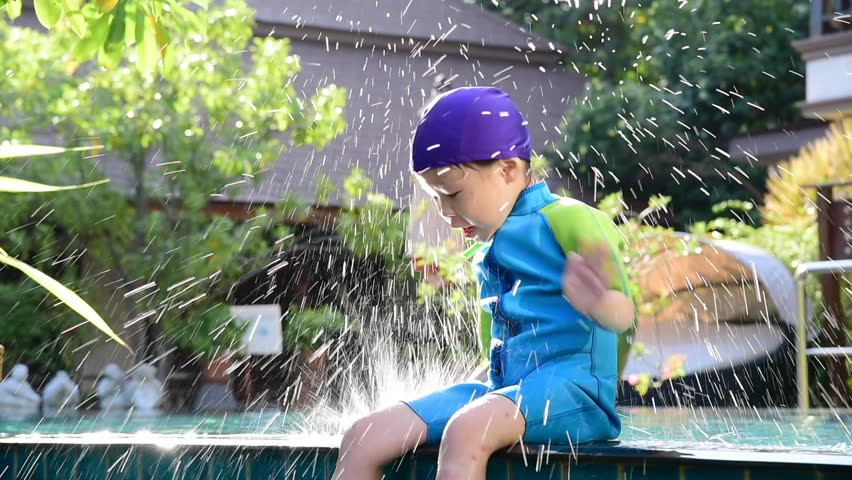 Little asian girl wearing swimsuit sitting at swim pool and playing with a water splash