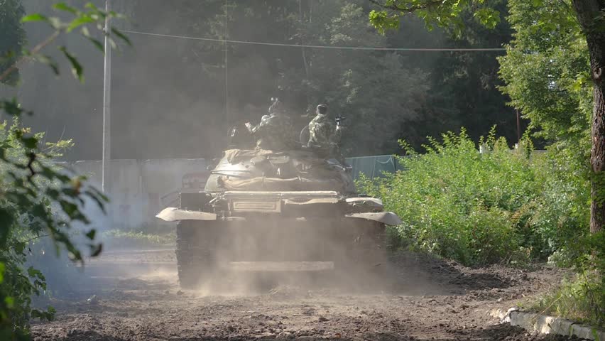 Military soldiers sitting on war tank moving on road view from back. War tank with soldiers driving on shooting range slow motion