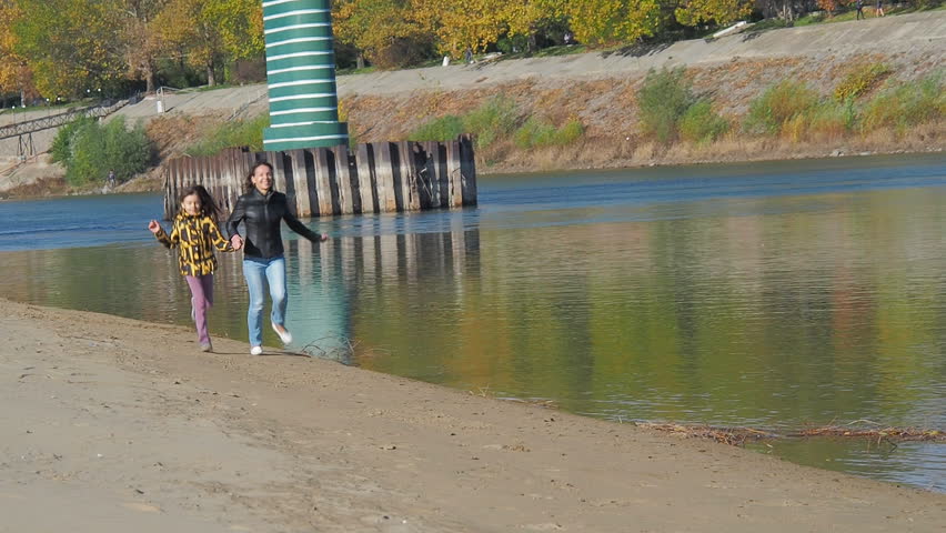 Happy family in nature. Mom and daughter are running along the river.