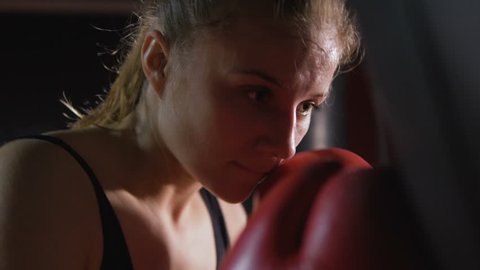 A girl is a boxer. The girl is training in the boxing hall. The girl is beating a punching bag.