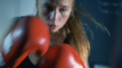 A girl is a boxer. The girl is training in the boxing hall. The girl is beating a punching bag.