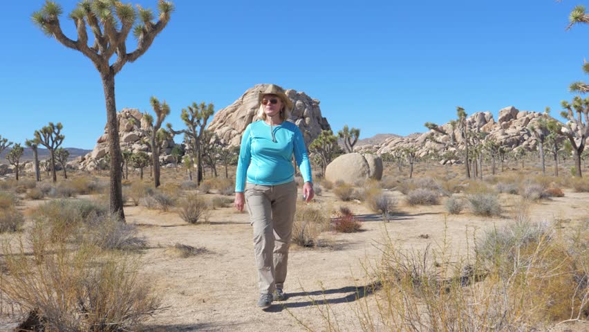 Mature happy woman in a cowboy hat, sunglasses and protective outdoor clothing. Is the Mojave desert, waving his hand in greeting. Front view, slow motion, 4K. Joshua Tree National Park, America, CA.