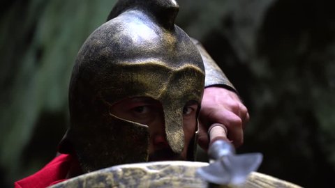 Closeup of a mature spartan soldier wearing a helmet hiding behind his shield looking to the camera fiercely holding a spear ready to fight bravery confidence masculinity concept.