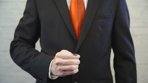 Flipping the coin and catching on top of hand 4K. Long shot of businessman with a red tie from shoulders to waist and hands holding a coin in focus. Shoot on an office wall background.