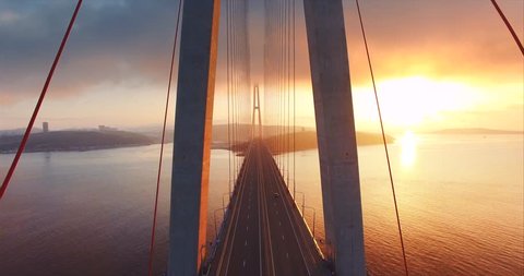 Flying above the road and between cables of cable-stayed Russian bridge across the Eastern Bosphorus strait on the way to Russian island in Vladivostok. Amazing sunrise. Aerial