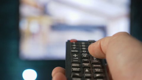 Close up mans hand holding TV remote control and changing TV channels. Blurry background