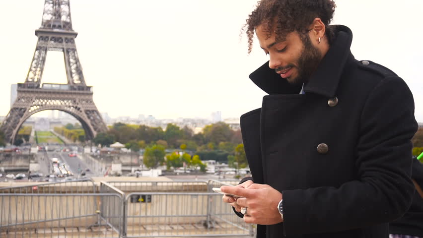 Young man dressed in black coat, has earing, black curly hair and beard. Concept of Internet innovations