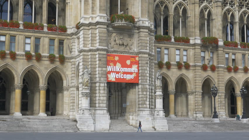 Static shot of woman going through main entrance of Rathaus in Vienna, Austria. Big sign Welcome above entrance