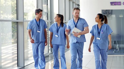 Medical Interns Wearing Scrubs Walk Towards Camera in Busy Hospital - Βίντεο στοκ