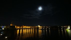 Time-lapse of Prague street with the national theater at night time with lights reflection in the river and full moon