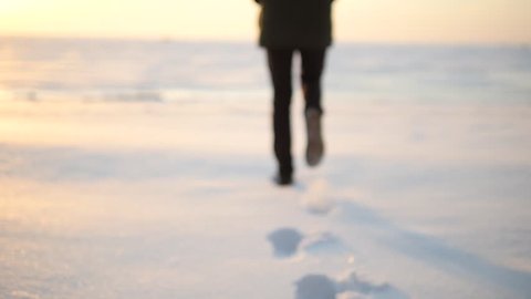 Legs of man walking on snow with footprints on snowy day