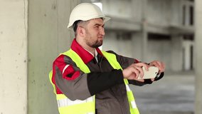 Builder at construction site records videos on smartphone. Worker in white hard hat with smartphone at project site