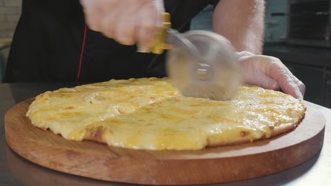 Chef in gloves cutting hot ready pizza by rolling pizza cutter, close-up slow motion