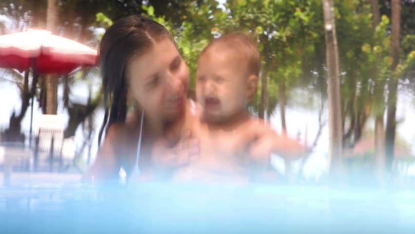 Happy young mother sitting and playing with her daughter in  swimming pool