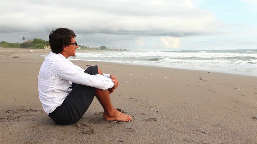 Businessman sitting on beach and looking at ocean  