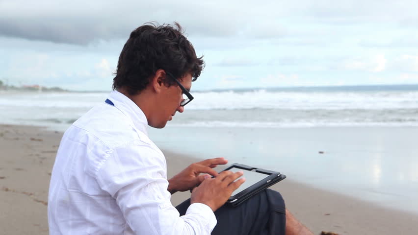 Businessman working on tablet pc at beach 