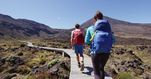 Travel adventure people. Young couple backpackers hiking on tramping track at Tongariro National Park in New Zealand. Male and female hikers with backpacks by Mount Ngauruhoe. Travel summer vacation.