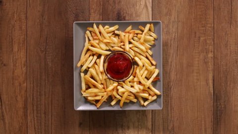 Hands taking french fries from a rotating plate - dipping it in ketchup, time lapse footage, fast food concept