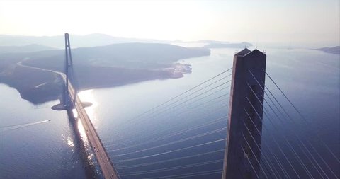 Ascending aerial view above the bridge pillar of cable-stayed Russian Bridge across the Eastern Bosphorus strait and Russky island under the bright sun. Vladivostok, Russia