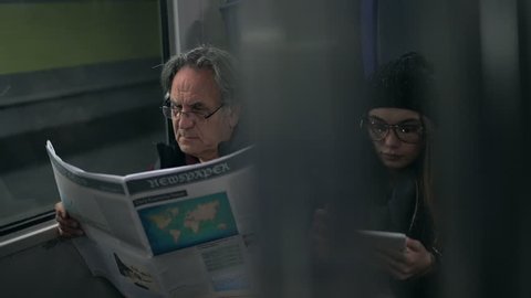 Passengers reading newspaper with using tablet in the metro