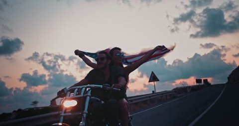 Young woman riding motorcyle with macho boyfriend holding American flag and celebrating fourth of July