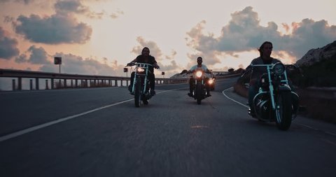 Group of young male motorcyclists riding vintage motorcycles on mountain highway at sunset ஸ்டாக் வீடியோ