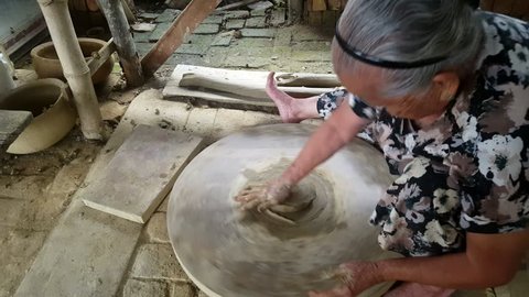 HOI AN/VIETNAM - OCTOBER 15 2017: Closeup grey-haired asian woman sits and makes earthenware crockery rotating special wooden wheel on October 15 in Hoi An