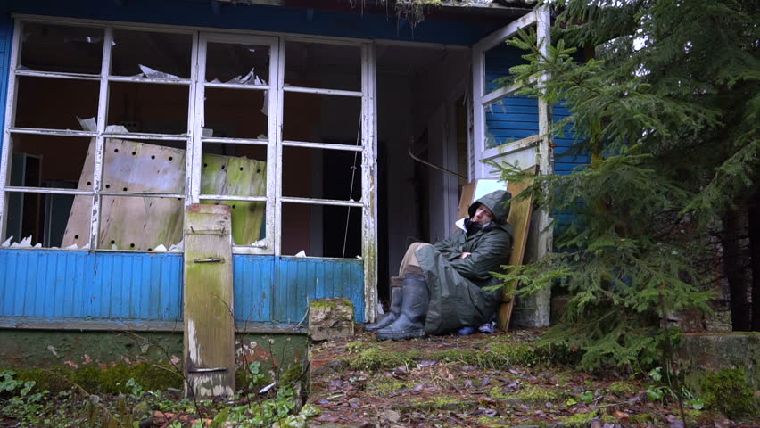 Homeless man sleeping in the open air on the porch of an abandoned ruined house