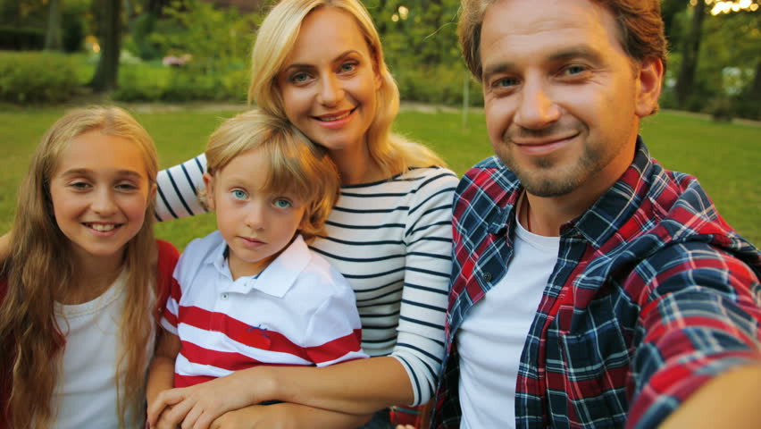 Smiling parents with their kids sitting on the green grass, waving their hands and having video chatting. POV. Portrait | Shutterstock HD Video #33288184