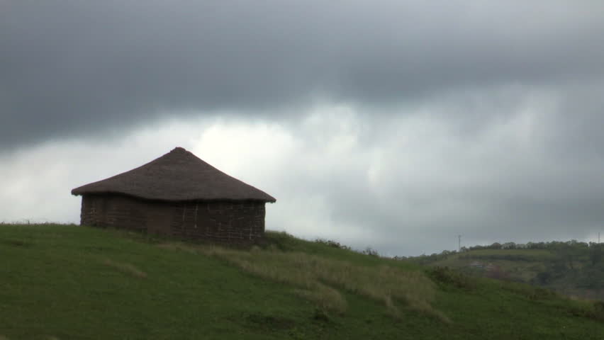 A silhouetted Xhosa hut ion a hill n the Transkei with dark rain clouds.