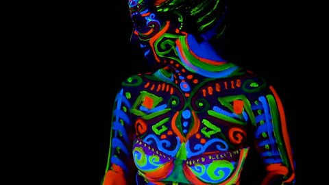 Beautiful young sexy girl in lingerie push up her breast with ultraviolet paint on her body. Girl with neon bodyart in color light.