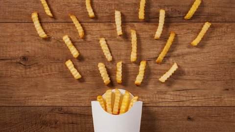 French fries falling into and pouring out of paper holder on brown wooden table - stop motion animation
