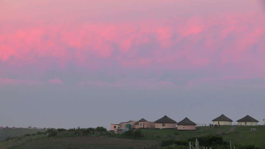 Wide of Xhosa huts with pink clouds at sunset.