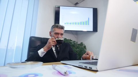 Businessman drinks coffe while watching the laptop screen