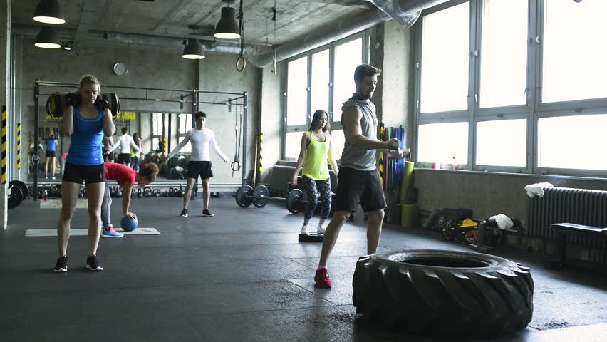 Young people in crossfit gym working out with various equipment.