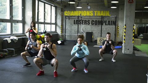 Young people in crossfit gym doing squats with kettlebells