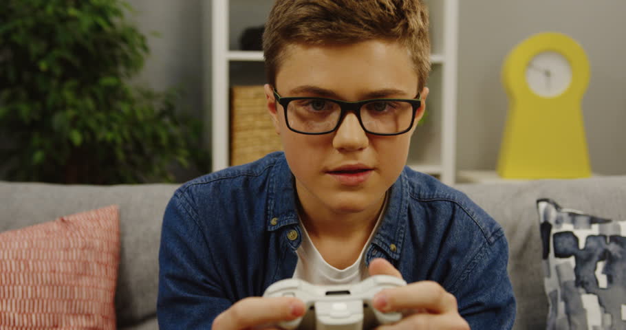 Close up of the teenager in glasses playing video games with a game control in his hands in the cozy room at home. Inside. Portrait shot | Shutterstock HD Video #33316549