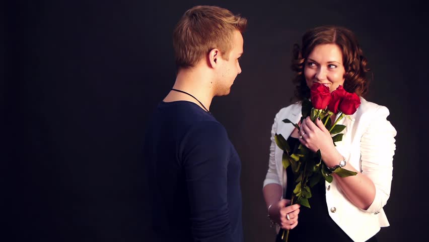 young man presents red roses wor a woman whos waiting for him