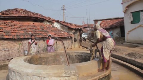 An old or elderly ethnic woman or lady in traditional attire or costume pulling water out of the water well in a rural Indian town or village 
