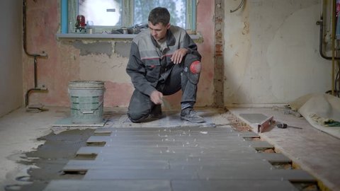 The worker in the building form checks the level of the surface on the ceramic tile, then puts the cement on the floor and combines the new floor element