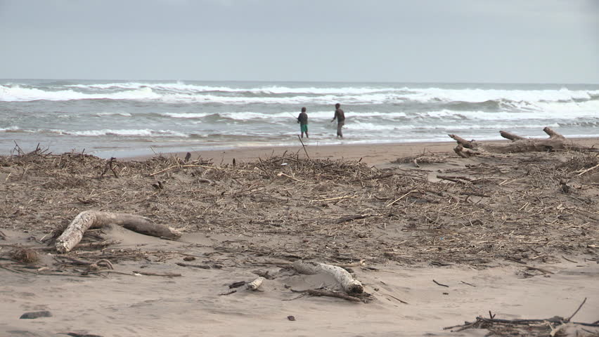 Beach with two African kids fishing. There's lots of wood debris in the
