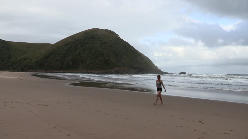 Young woman walking on Manteku beach, smiles and waves to camera.