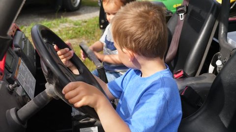 Two little boys play with the steering wheel on a side by side four wheeler